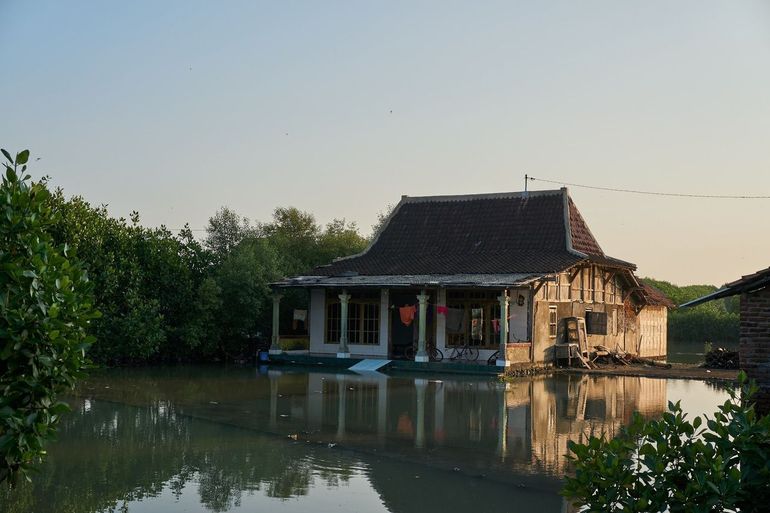 House in a coastal village during a high high tide. The plot is largely flooded, but the house has been raised significantly by the inhabitants in the last years