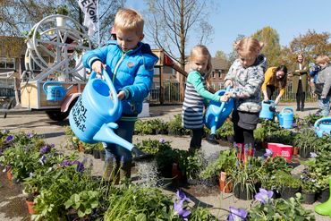 Kinderen geven plantjes water tijdens de viering van het 100ste groene schoolplein