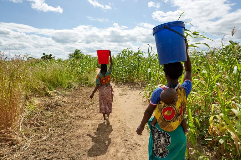 Gemeenschapsleden wandelen met zojuist gehaald water naar huis, Chikolongo, Malawi. De rivier de Shire was generaties lang de enige waterbron voor de dertien dorpen die samen de Chikolongo-gemeenschap vormen
