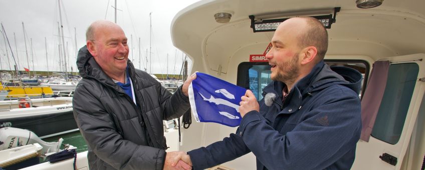 Schipper Sjef Mathijssen (links) ontvangt de eerste steurenvlag van Bram Houben van ARK Natuurontwikkeling