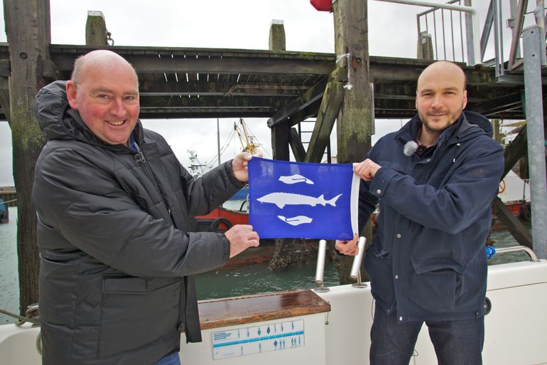 Schipper Sjef Mathijssen (links) ontvangt de eerste steurenvlag van Bram Houben van ARK Natuurontwikkeling