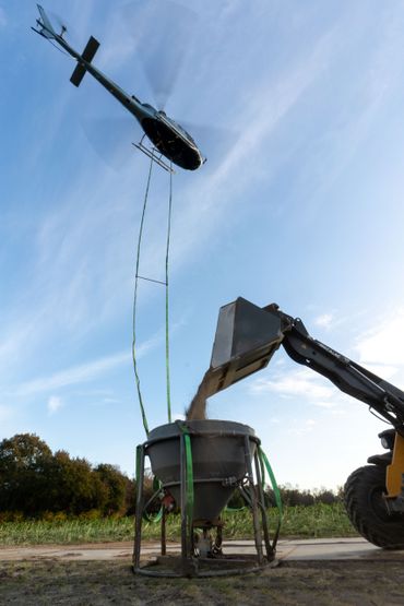 De bak met gruis hangt twintig meter onder de heli tijdens het verspreiden