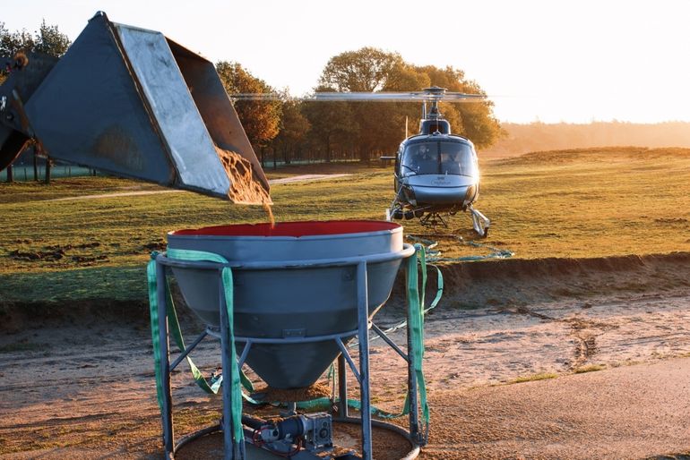 De helikopter haalt het schelpgruis op om te verspreiden